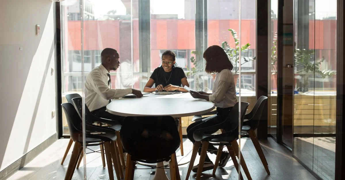Tres profesionales colaborando en un moderno salón de reuniones durante el día.
