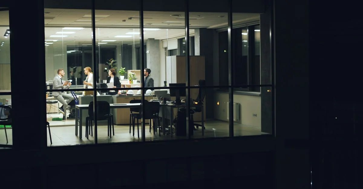 Una reunión nocturna en una oficina con profesionales trabajando en una moderna oficina con paredes de vidrio.