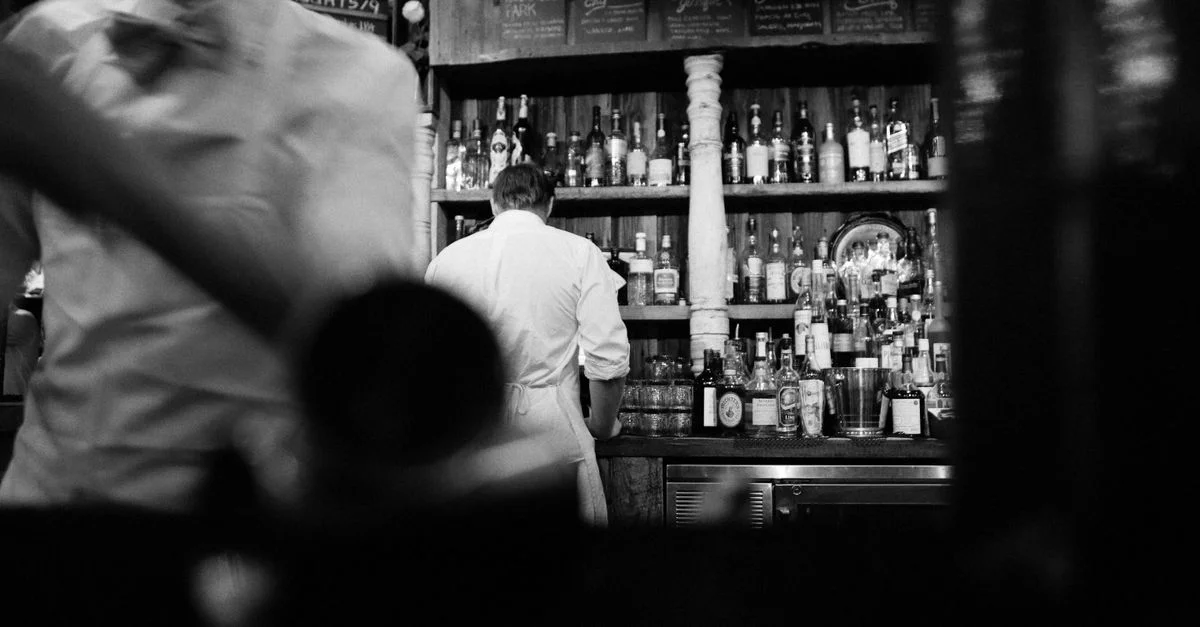 Una foto en blanco y negro que captura a los camareros trabajando en un bar vintage.
