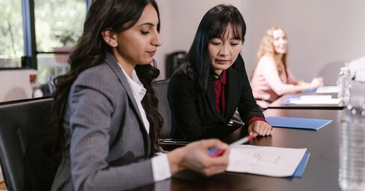Dos mujeres de negocios discutiendo documentos en una reunión corporativa en un entorno de oficina.