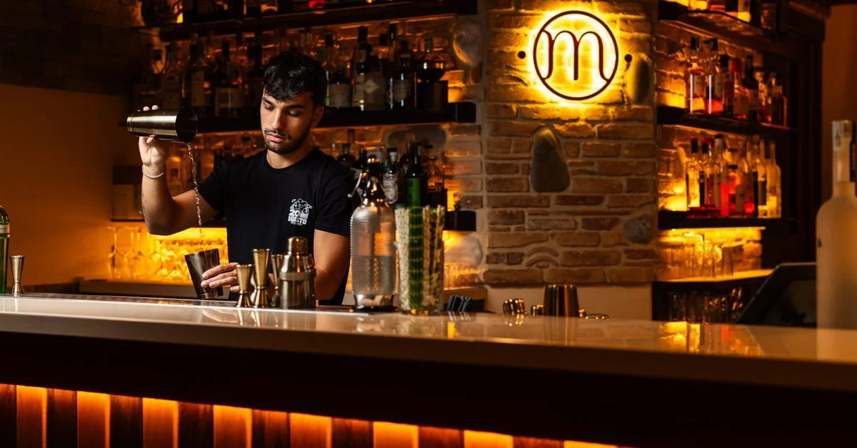 Un camarero prepara con maestría cócteles en un bar elegante y con luz tenue, creando un ambiente cálido y acogedor.