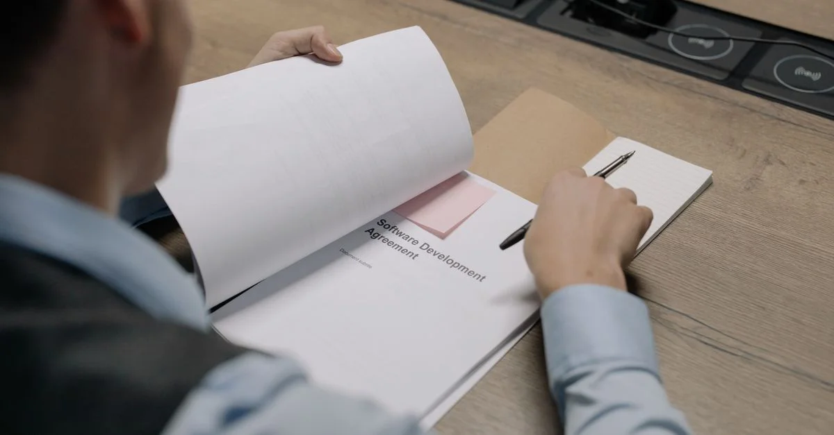Profesional de negocios en el escritorio examinando un documento de acuerdo de desarrollo de software.