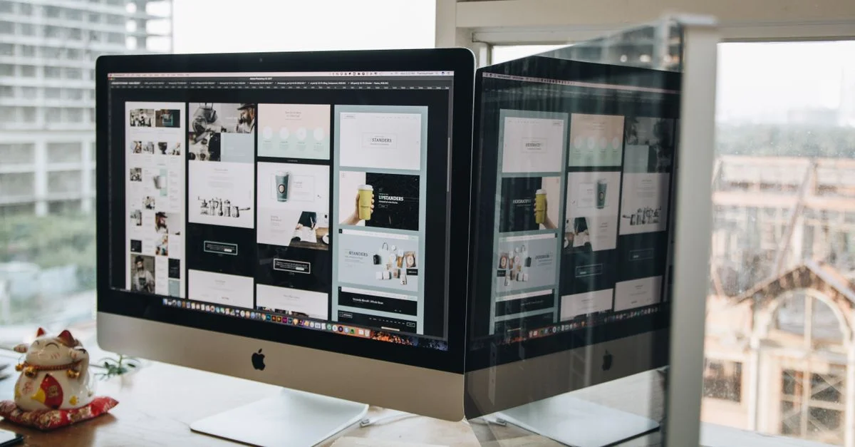 Monitores dobles en un escritorio, mostrando diseño web en un entorno de oficina moderna.