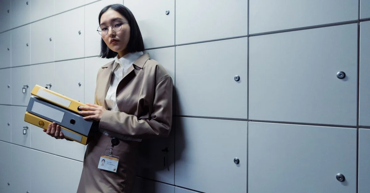 Mujer de negocios en atuendo de oficina de pie con documentos, luciendo segura en un entorno de oficina moderno.