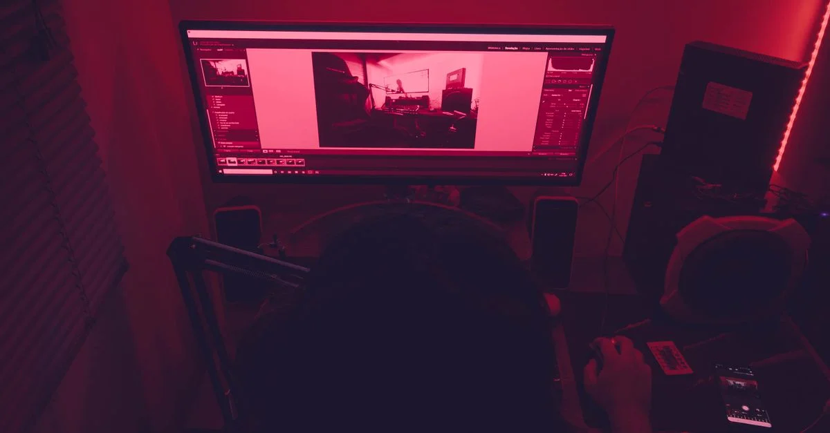 Un escritorio iluminado en rojo con un hombre trabajando en una computadora por la noche, con elementos tecnológicos.